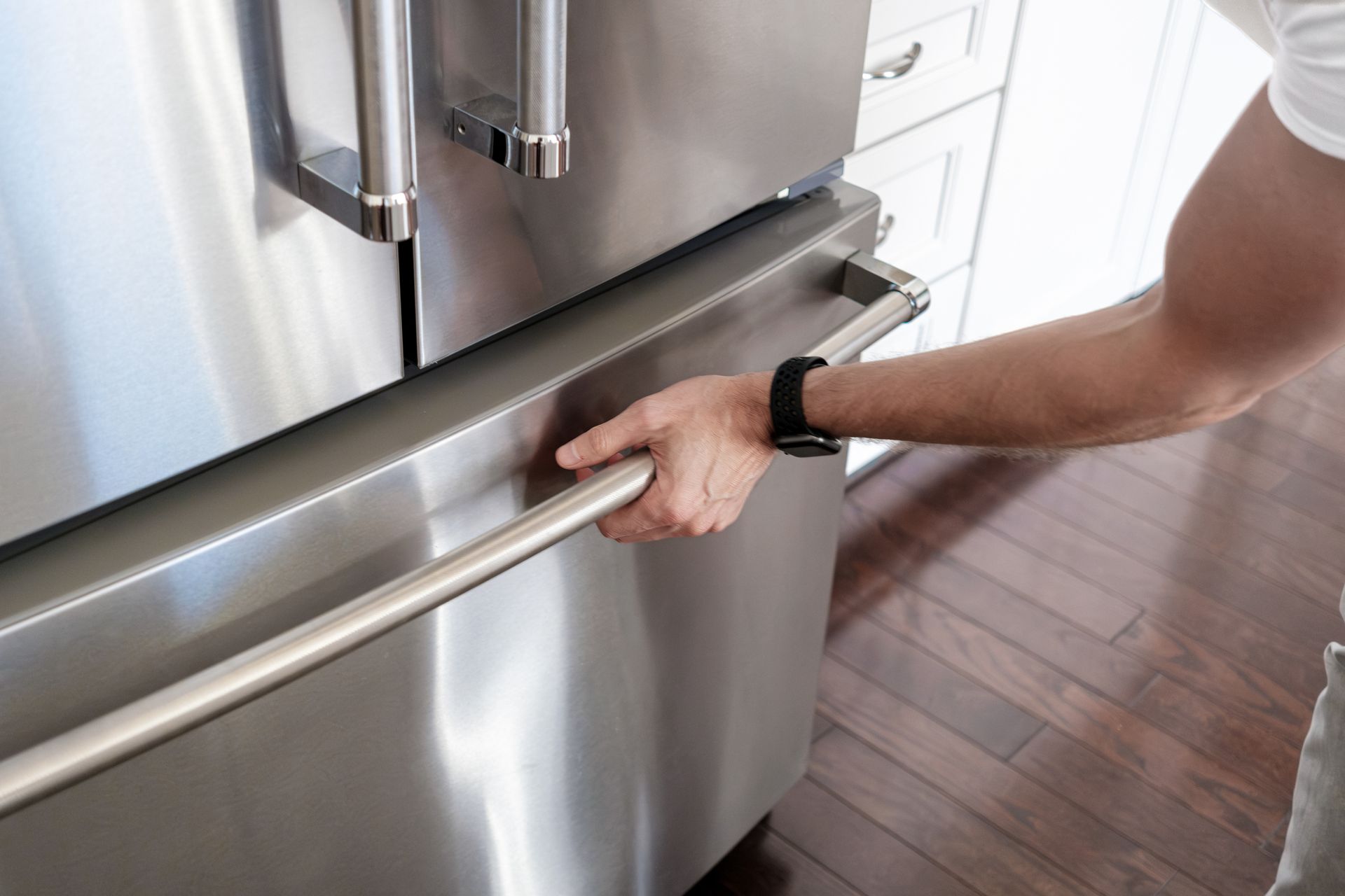 View of a man with a black watch opening the lower section of a refrigerator.