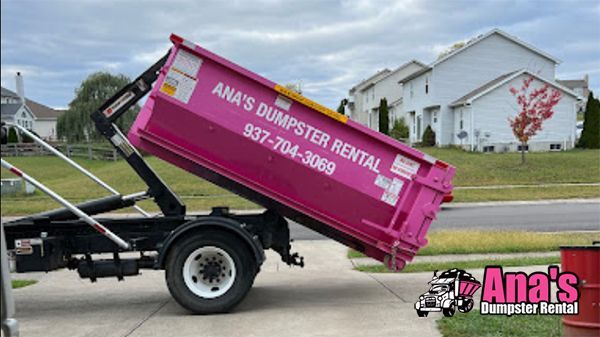 Pink Ana’s Dumpster Rental dumpster on a truck in a suburban street, being hauled away