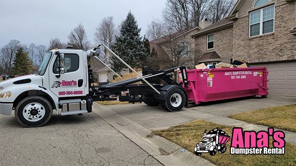 Dumpster truck loading a bright pink dumpster on a suburban driveway