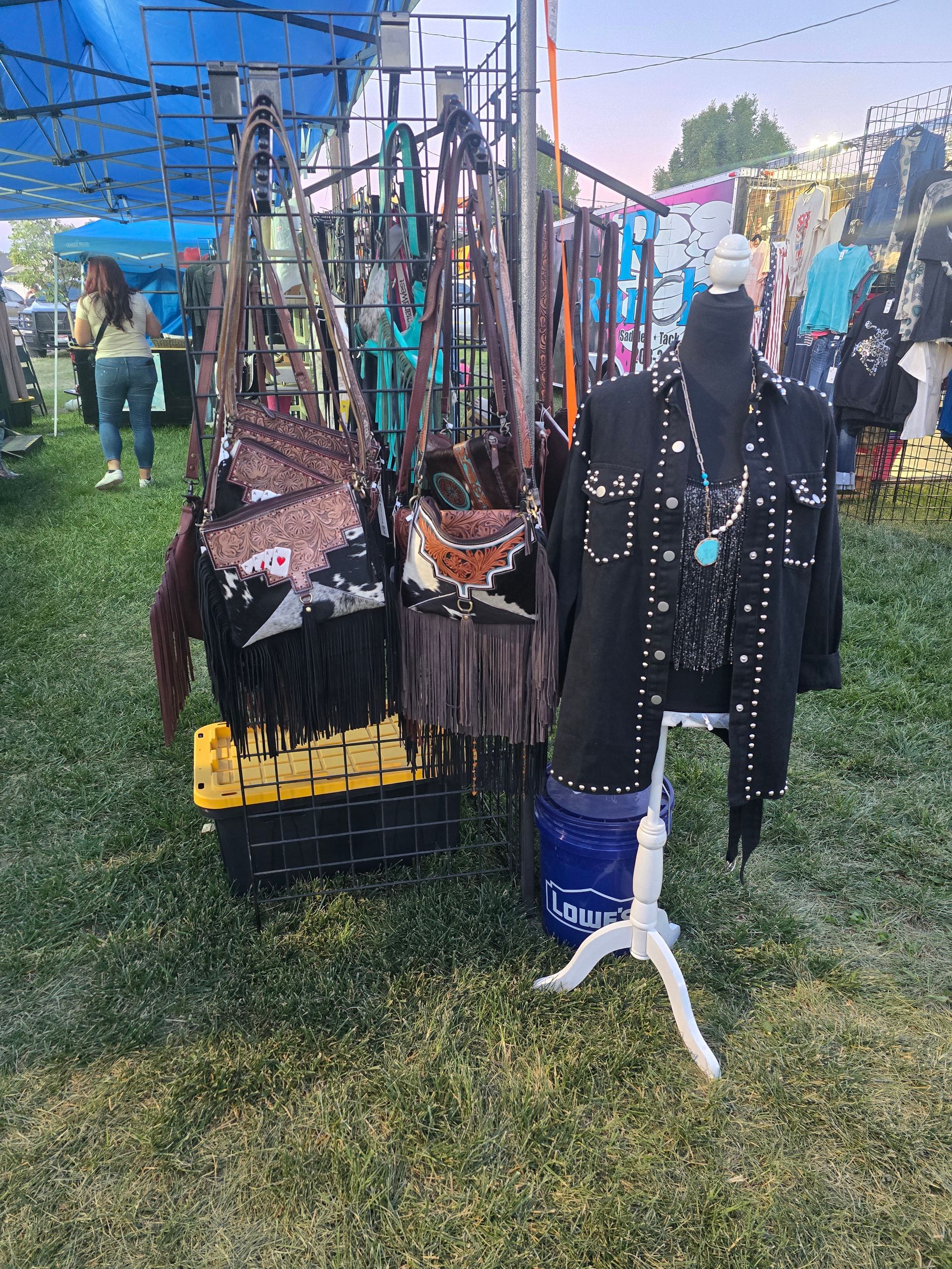 Booth displaying fringed handbags and studded black jacket on a mannequin at an outdoor market.