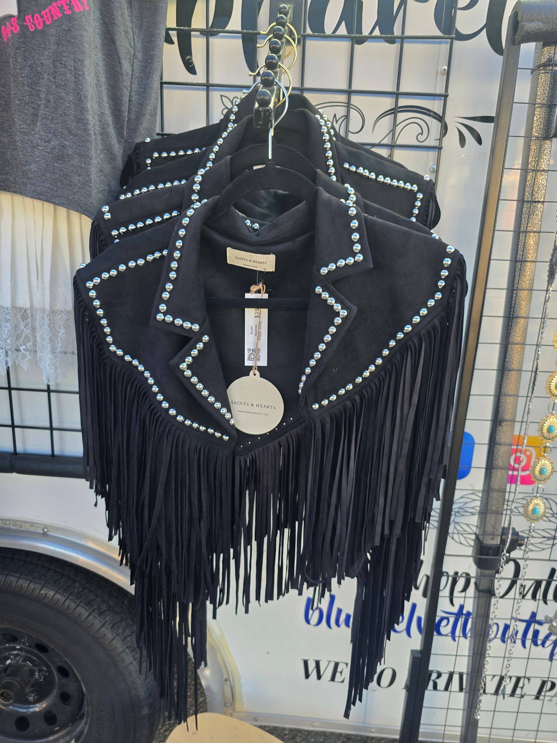 Black fringed jacket with silver studs hanging on a rack.