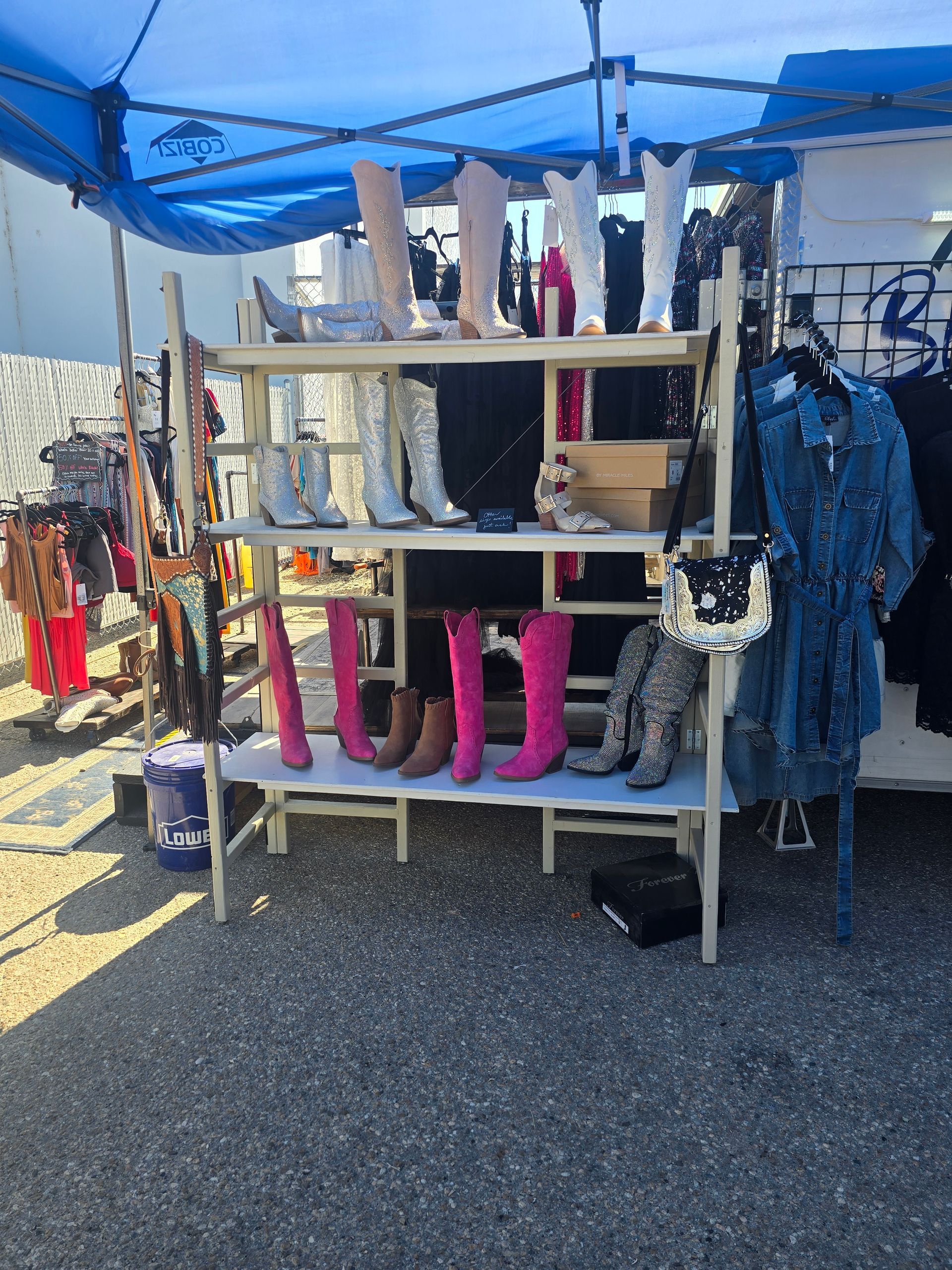 Boots for sale on shelves under a blue canopy at an outdoor market.