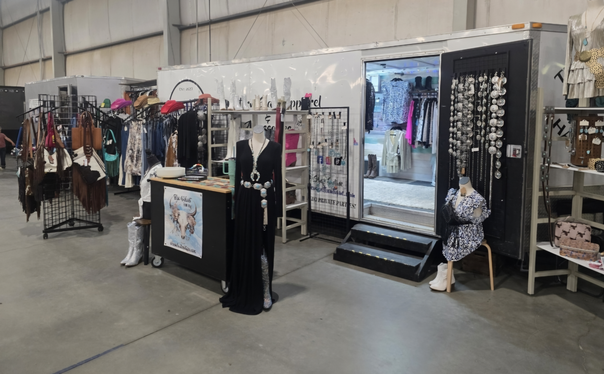 A fashion boutique inside a trailer, selling clothes and jewelry at an indoor event.