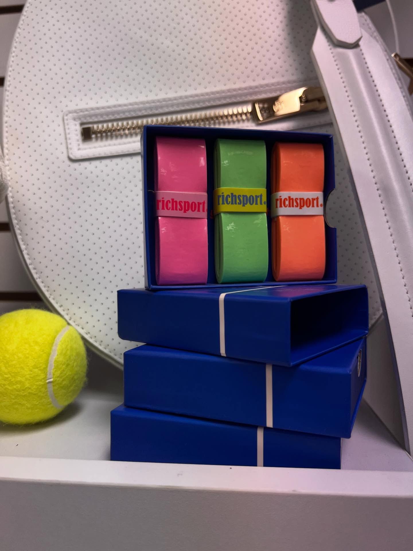 Blue stacked boxes with colorful lip balm tubes beside a yellow tennis ball and white bag