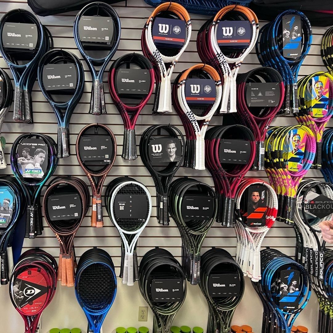 Assorted tennis rackets displayed in rows on a store wall, with black, red, and colorful frames.