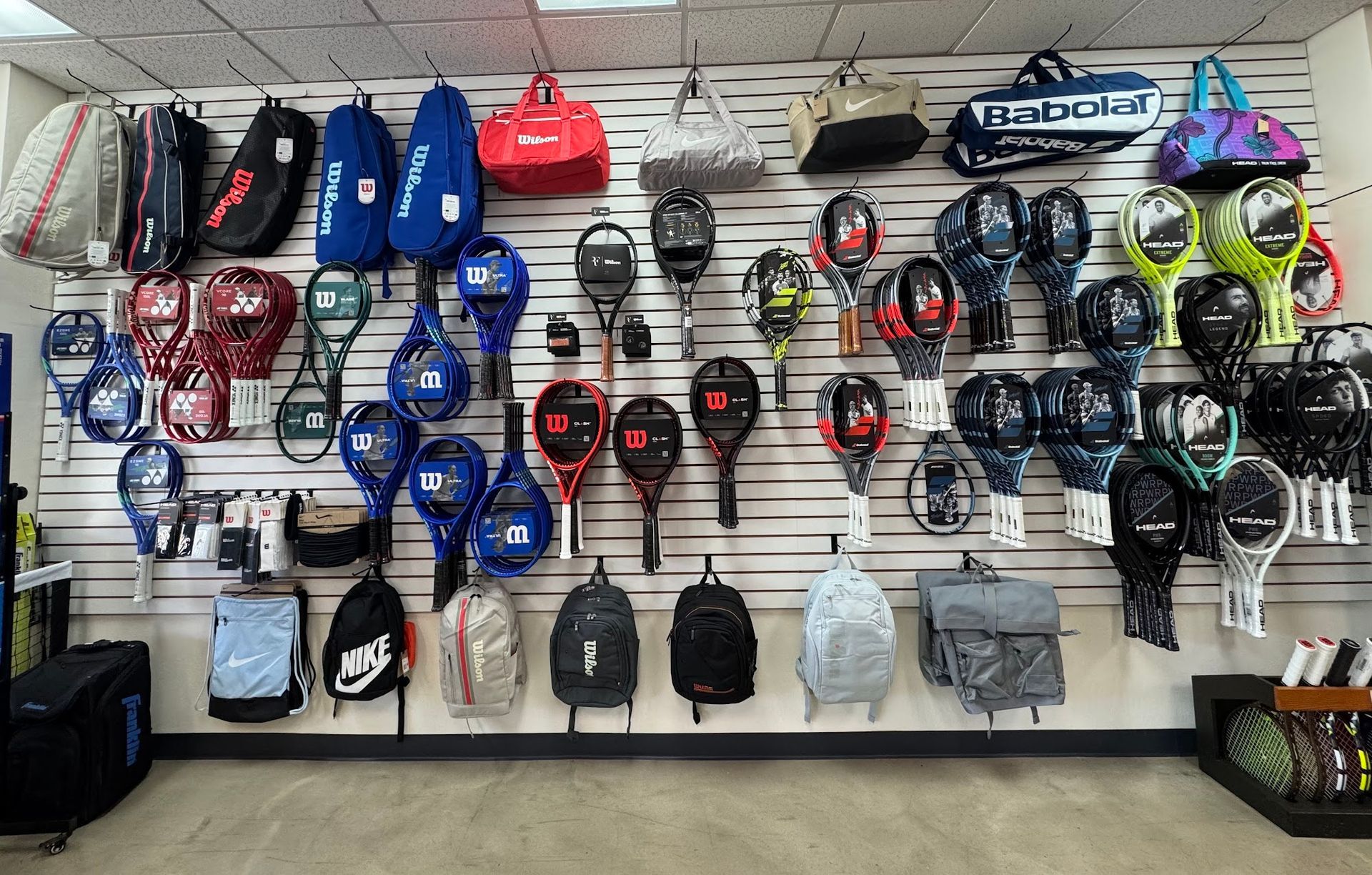 Wall display of assorted tennis rackets and accessories in a sports store, arranged by color and brand.