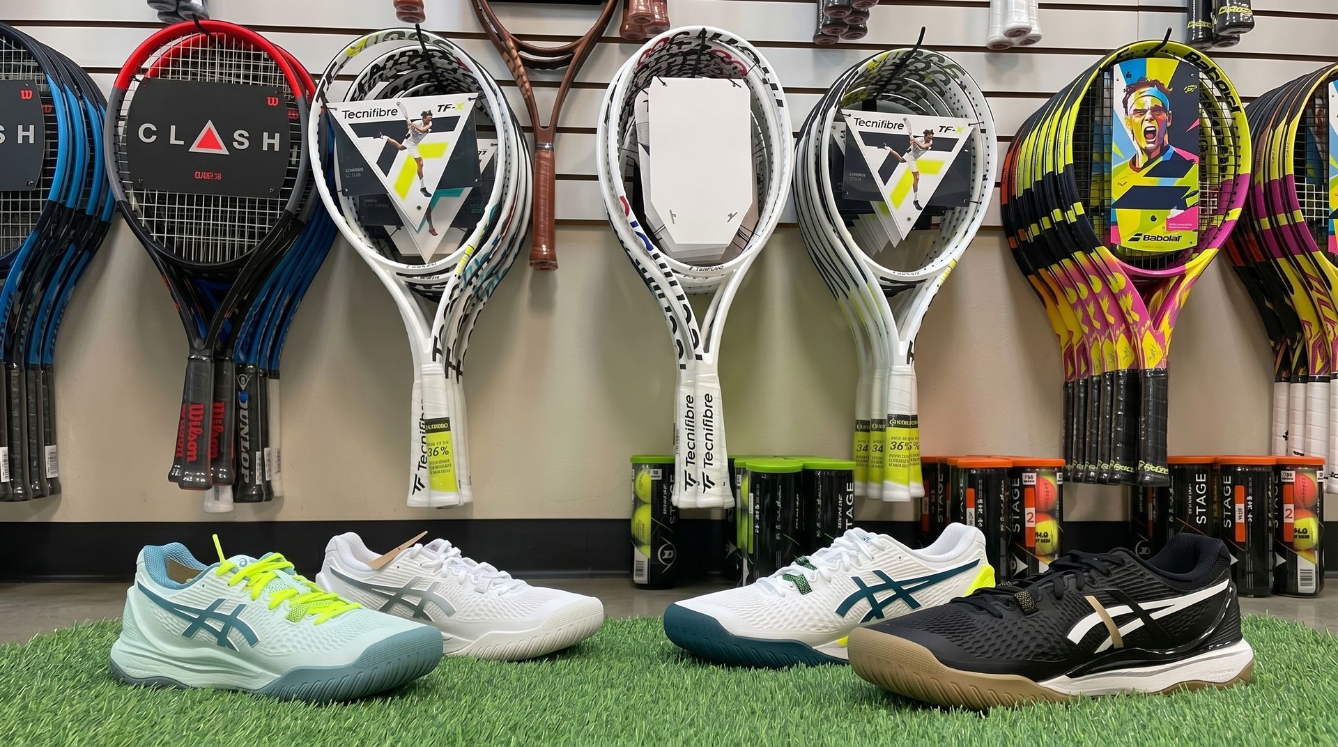 Tennis rackets on display above three pairs of tennis shoes on artificial turf.
