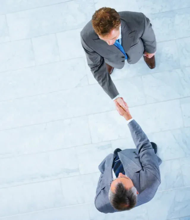Two businesspeople in suits shaking hands on a light blue office floor, viewed from above