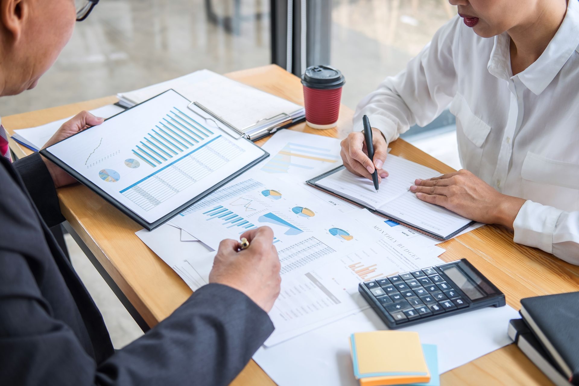 People reviewing financial charts and documents at a desk with a calculator and coffee cup