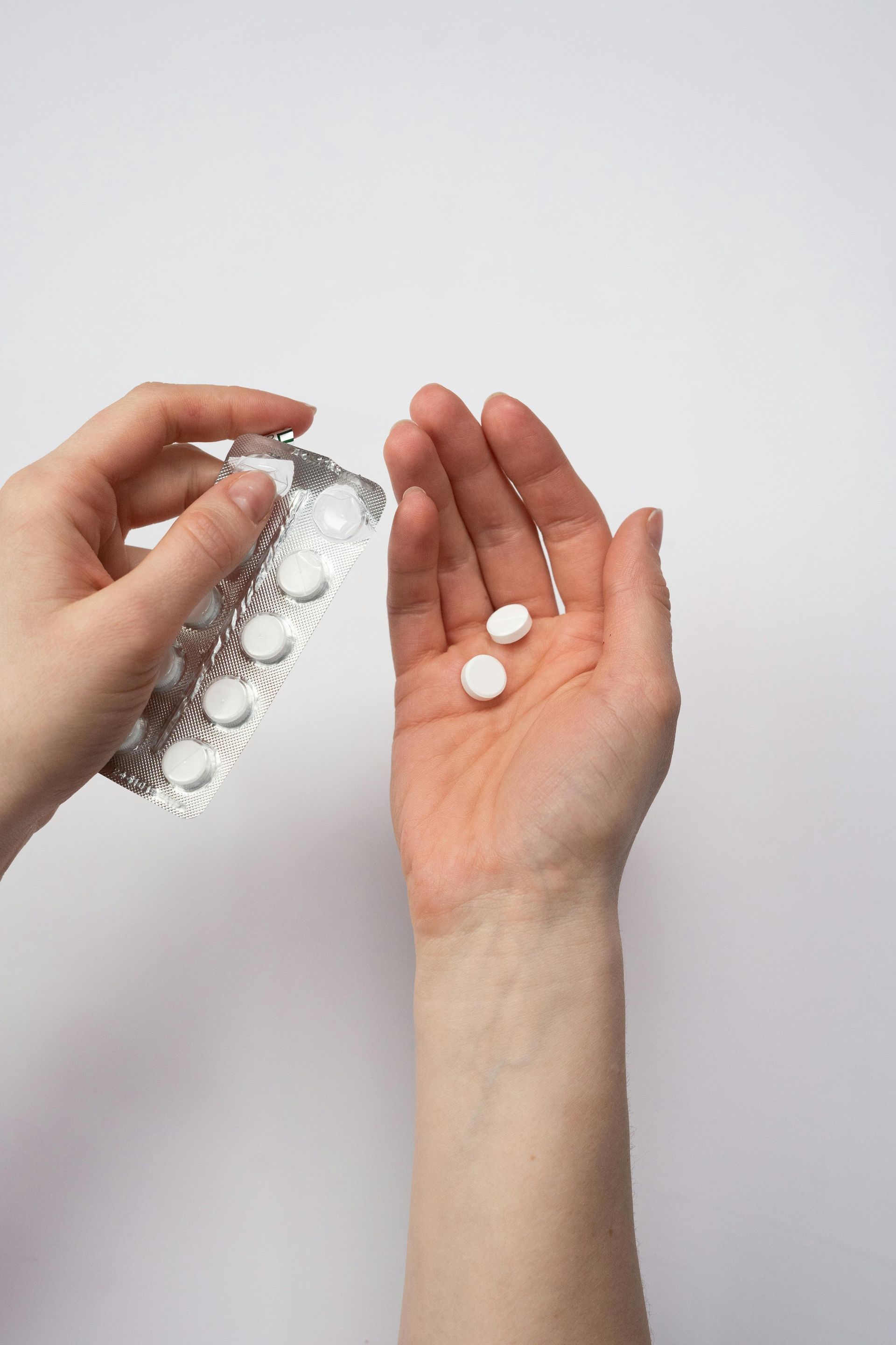 Hand dropping white pills from a blister pack into an open palm