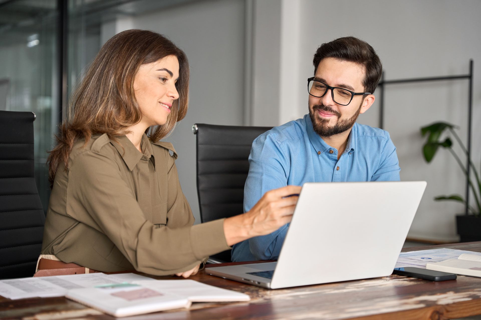 Two coworkers collaborating at a laptop in an office, one pointing at the screen