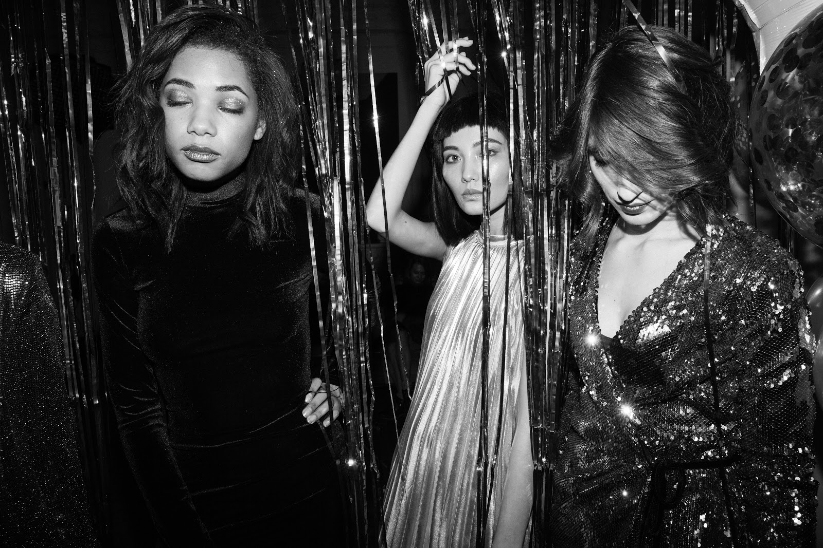Three women are standing next to each other in front of a tinsel curtain.