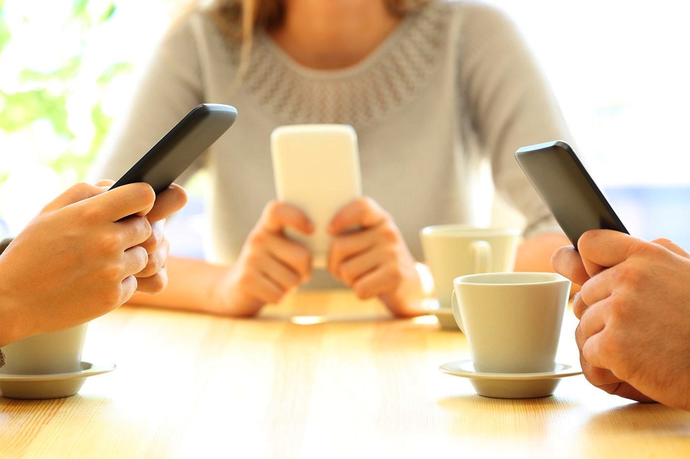 People at a table, each holding a smartphone. Two coffee cups present.