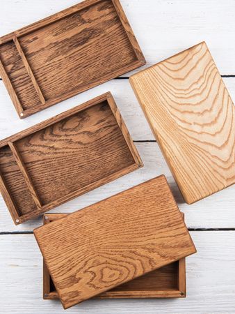 Tre scatole di legno con coperchi su una superficie grigio chiaro, che mostrano diverse venature del legno.