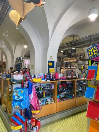 Bancarella al coperto con scaffali pieni di giocattoli e regali colorati sotto soffitti bianchi ad arco.