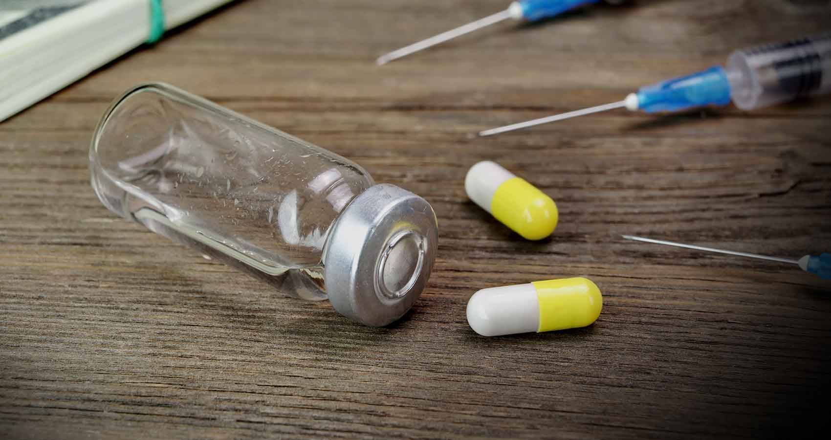 A bottle of pills and syringes on a wooden table.
