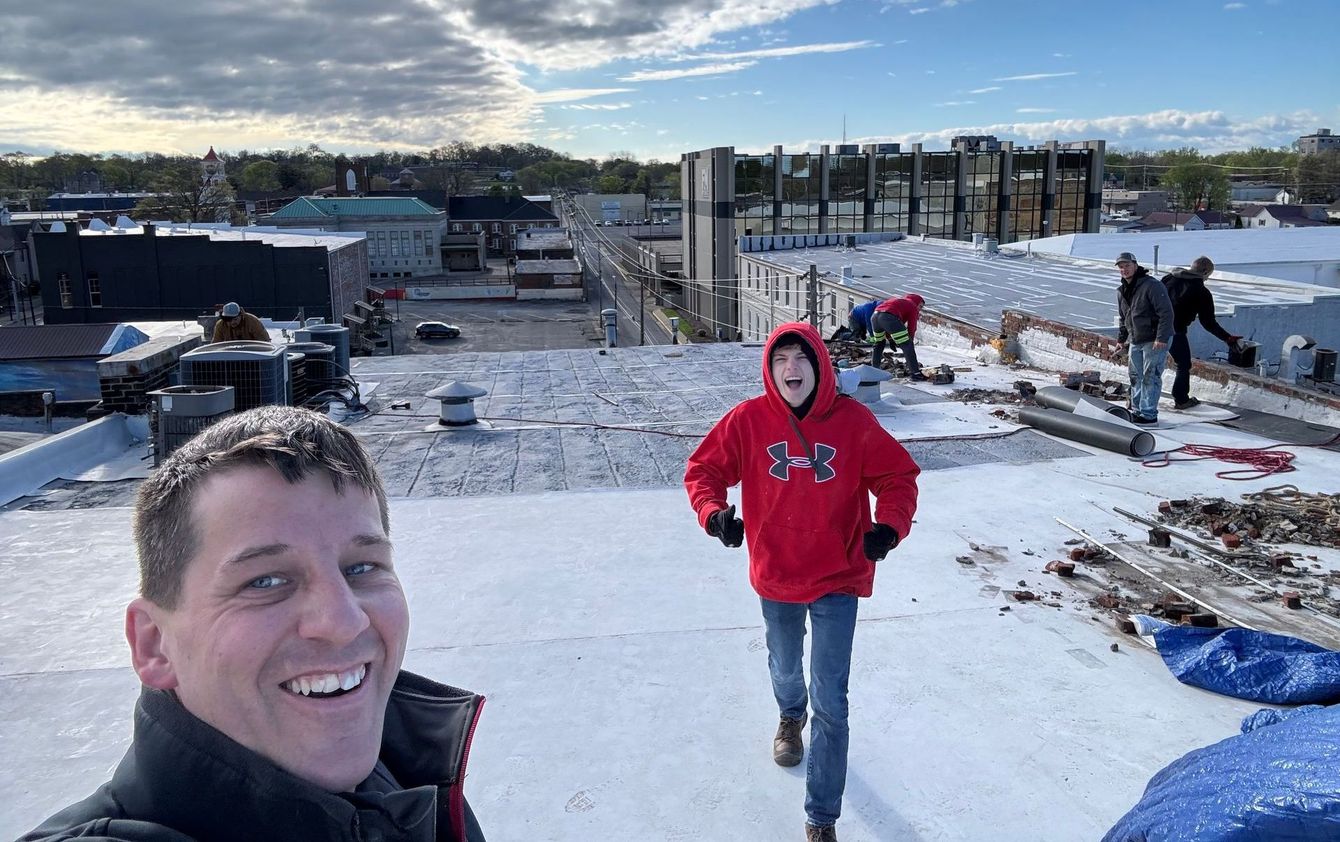 A man and a boy are standing on top of a snow covered roof.