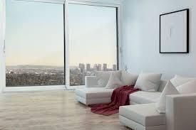 Soggiorno moderno con divano bianco, coperta rossa, ampia finestra, vista sulla città e opere d'arte incorniciate.