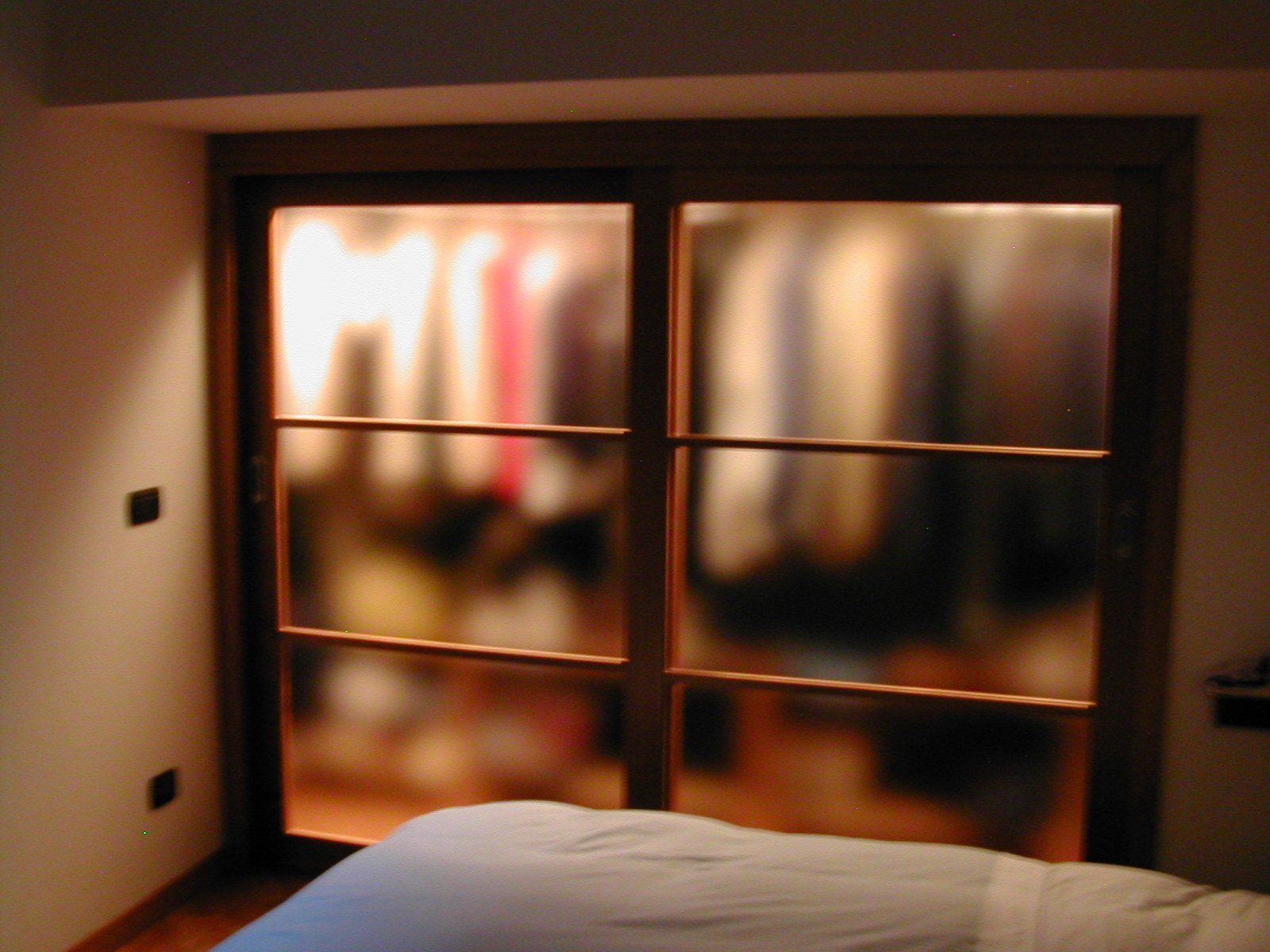 Porte scorrevoli in vetro dell'armadio con vista sfocata dei vestiti appesi, incorniciate in legno.