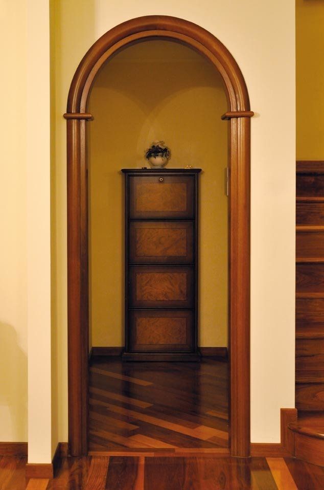 Un arco in legno incornicia un mobiletto contro una parete gialla, su un pavimento in legno.