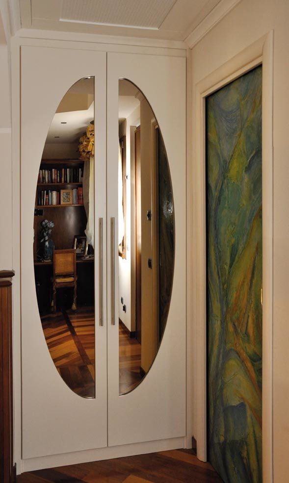 Armadio a muro bianco con specchi ovali e maniglie argentate. Un quadro è sulla destra.