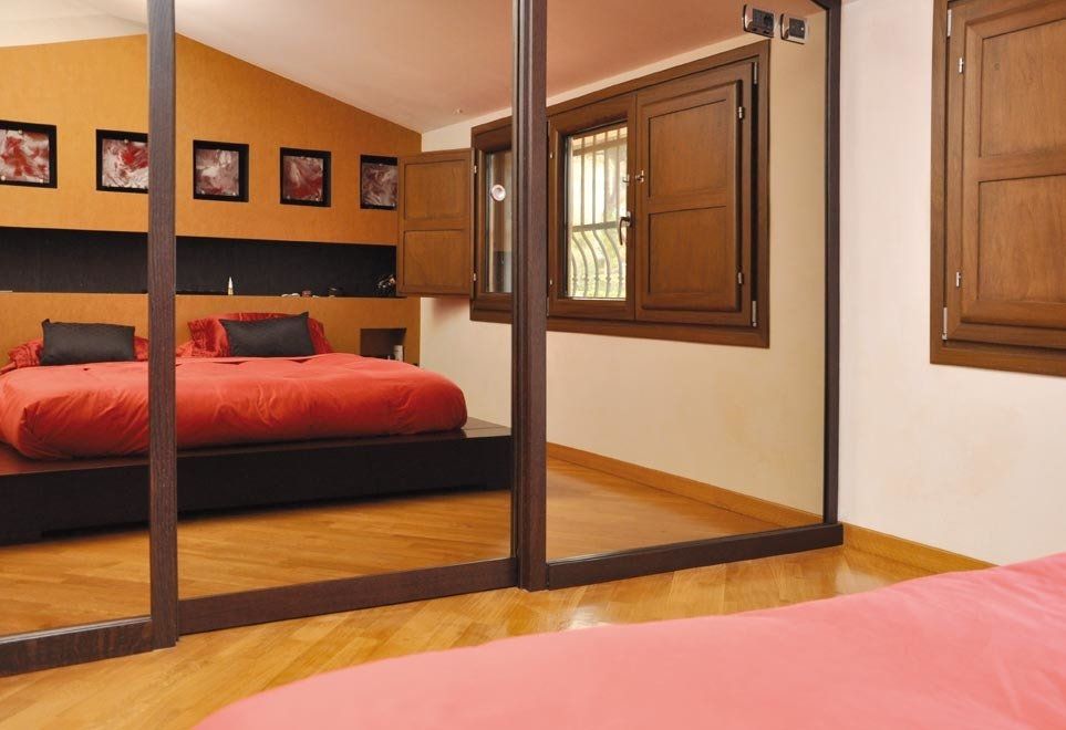 Camera da letto con ante dell'armadio a specchio che riflettono il letto, finestre e pavimento in legno.