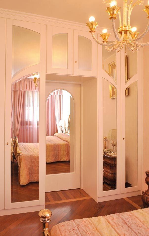 Armadio bianco con ante a specchio, che riproduce una camera da letto con letto e lampadario.