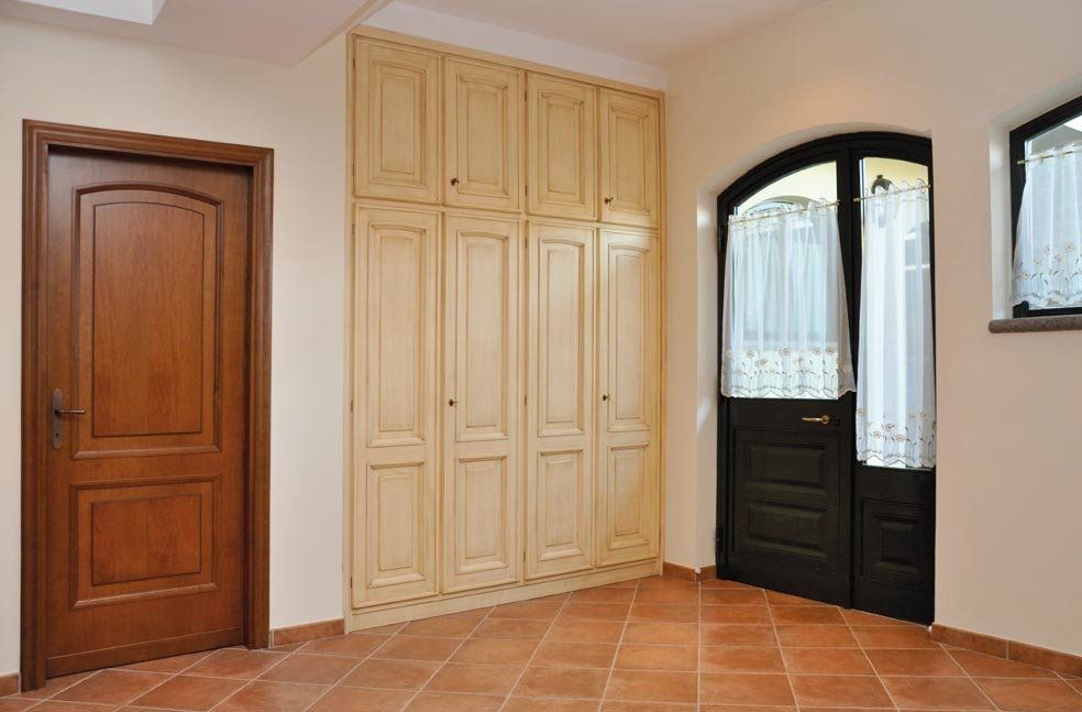 Vista interna con porte in legno, un grande armadio e una porta ad arco. Pareti beige e pavimento piastrellato.
