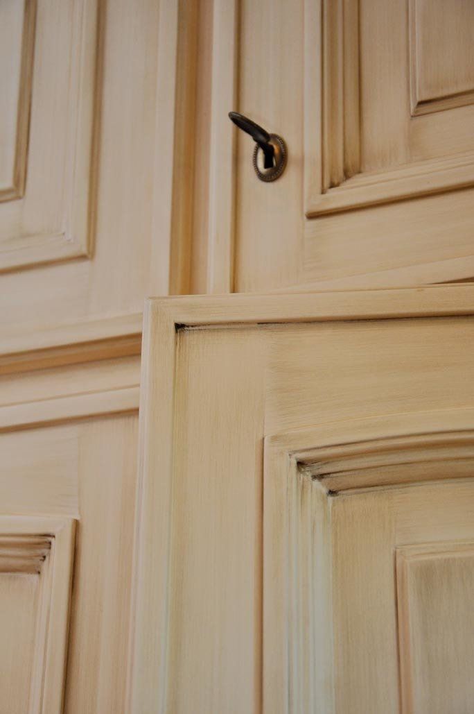 Primo piano di una porta in legno chiaro con maniglia scura, che mostra i pannelli e le finiture.