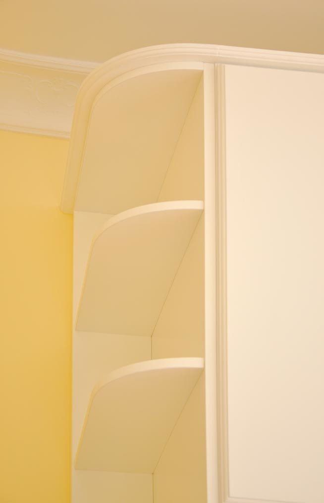 Scaffale bianco incorporato con piano curvo e ripiani triangolari contro una parete gialla.