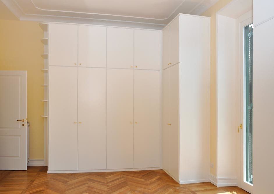 Armadio a muro bianco in una stanza con pareti gialle e pavimento in parquet.