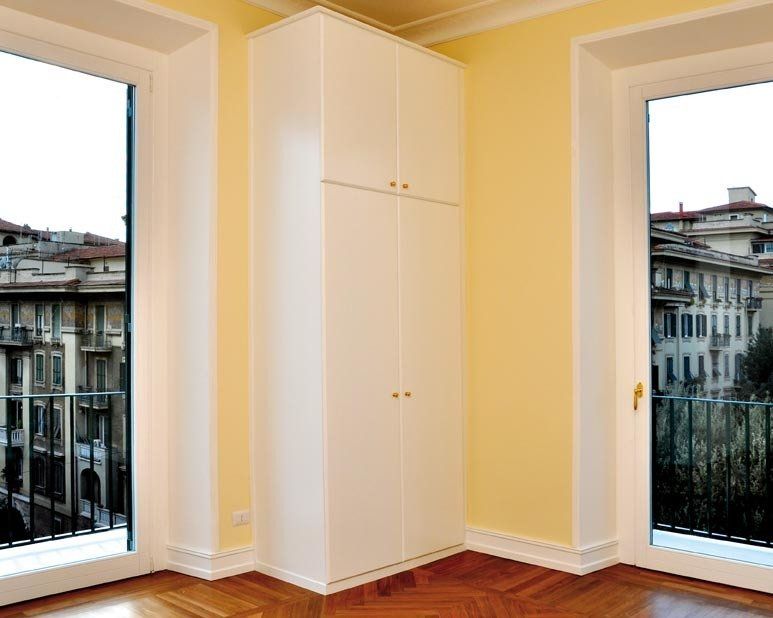 Mobile bianco in un angolo di una stanza con due finestre e vista sulla città. Pareti gialle, pavimento in legno.