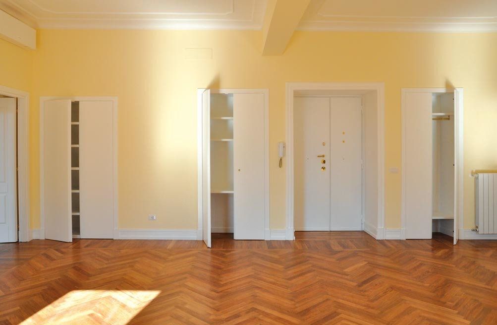 Stanza vuota con pareti giallo chiaro, pavimento in legno a spina di pesce e armadi bianchi a muro.