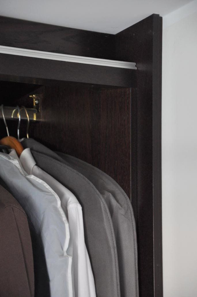 Primo piano di un armadio con ripiani in legno scuro e abiti appesi in varie tonalità di grigio e bianco.