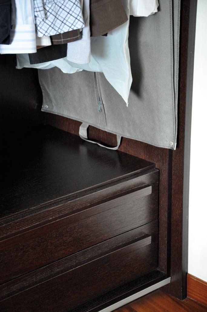 Primo piano dell'interno di un armadio in legno marrone scuro con cassetti e vestiti appesi.