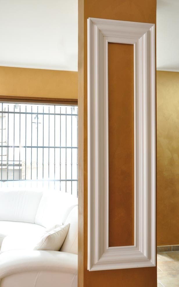 Un rettangolo con cornice bianca su una parete color ocra. Si vede una finestra con un divano bianco e sbarre di metallo.