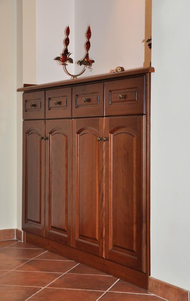 Mobile in legno con cassetti e ante, appoggiato a una parete bianca in un angolo. Pavimento in piastrelle rosso-marroni.