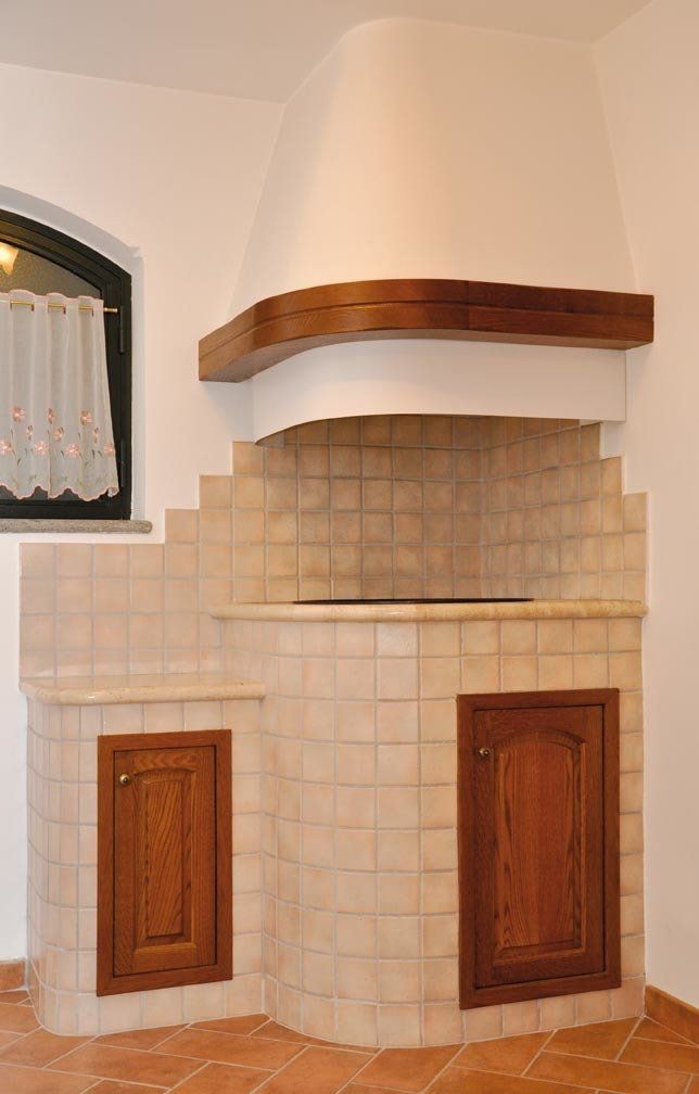 Angolo cottura piastrellato con mobili in legno, cappa aspirante e pavimento in cotto.