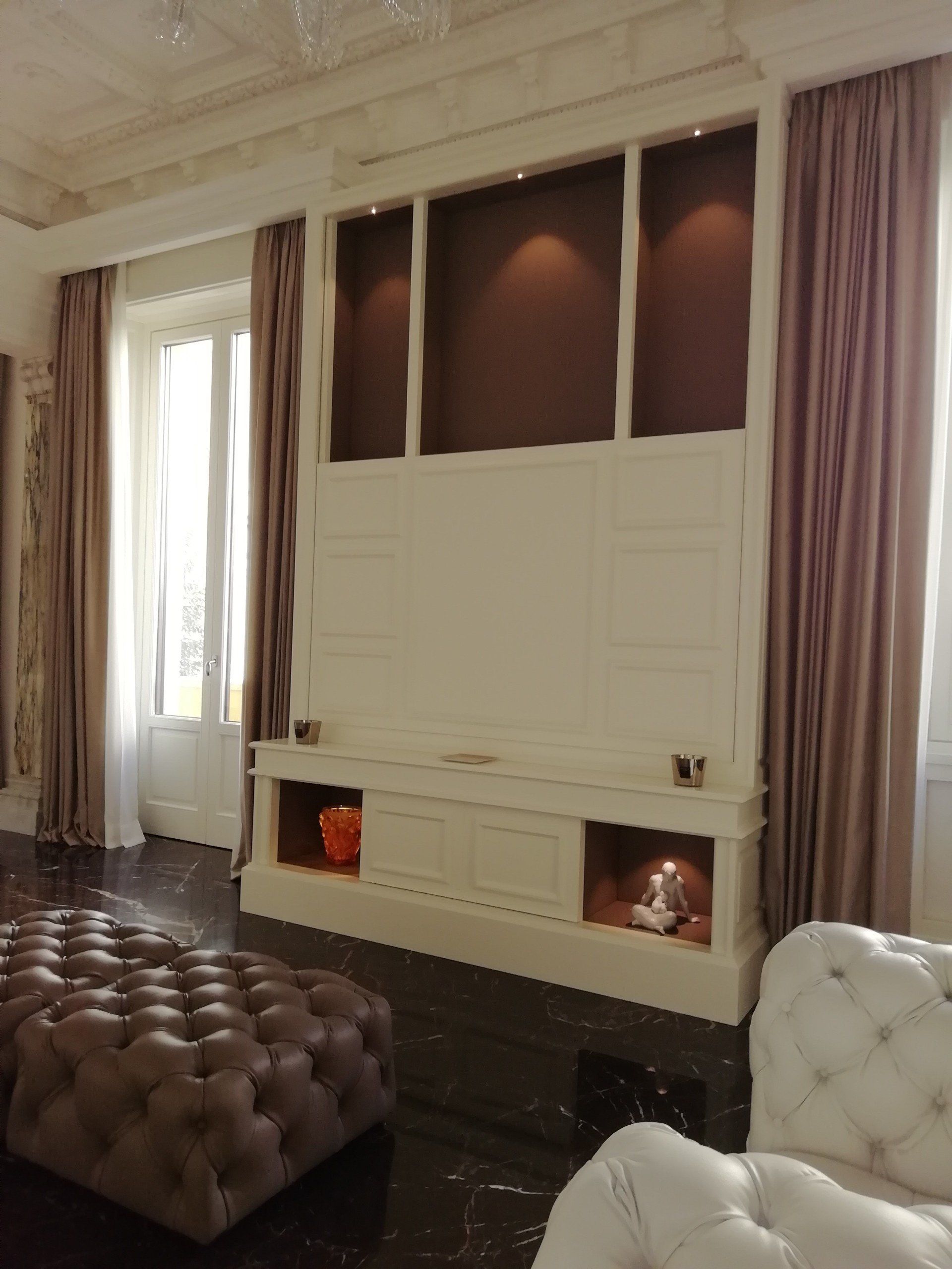 Soggiorno con centro di intrattenimento integrato, pareti marrone scuro, mobili beige, tende color malva e pouf imbottito.