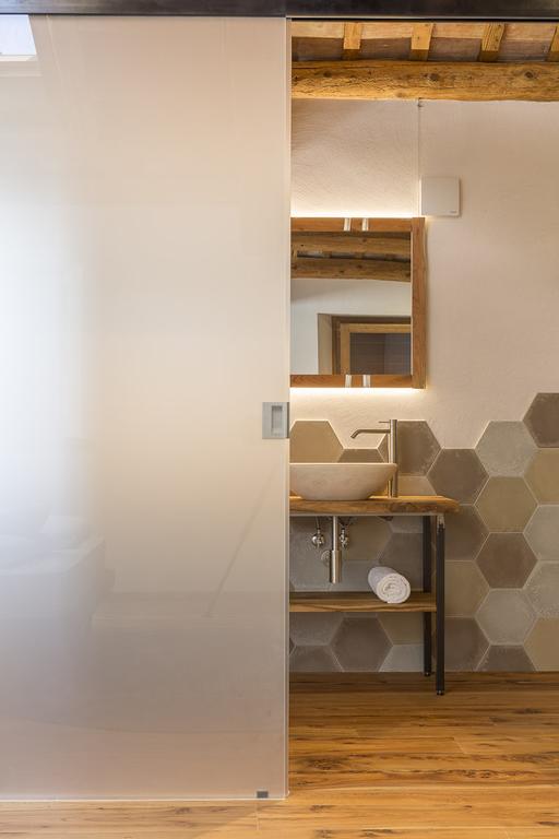 Bagno con porta scorrevole in vetro smerigliato, lavandino in pietra, ripiani in legno e metallo, parete decorativa con piastrelle esagonali.