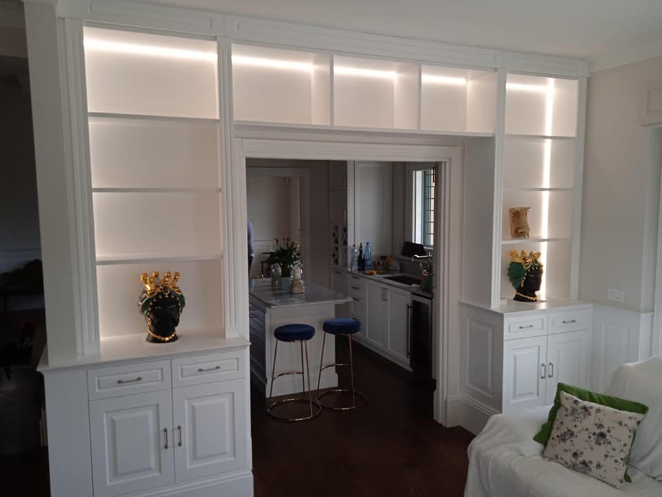 Mensole bianche integrate con illuminazione interna che incorniciano la porta di accesso alla cucina.