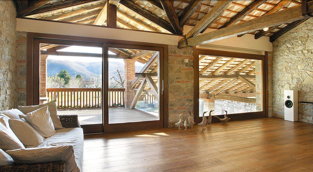 Soggiorno con pavimenti in legno, pareti in pietra, ampie finestre e balcone con vista sulle montagne.