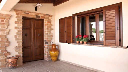 Esterno di una casa con una porta di legno marrone, dettagli in mattoni, finestra con persiane e ceramiche.