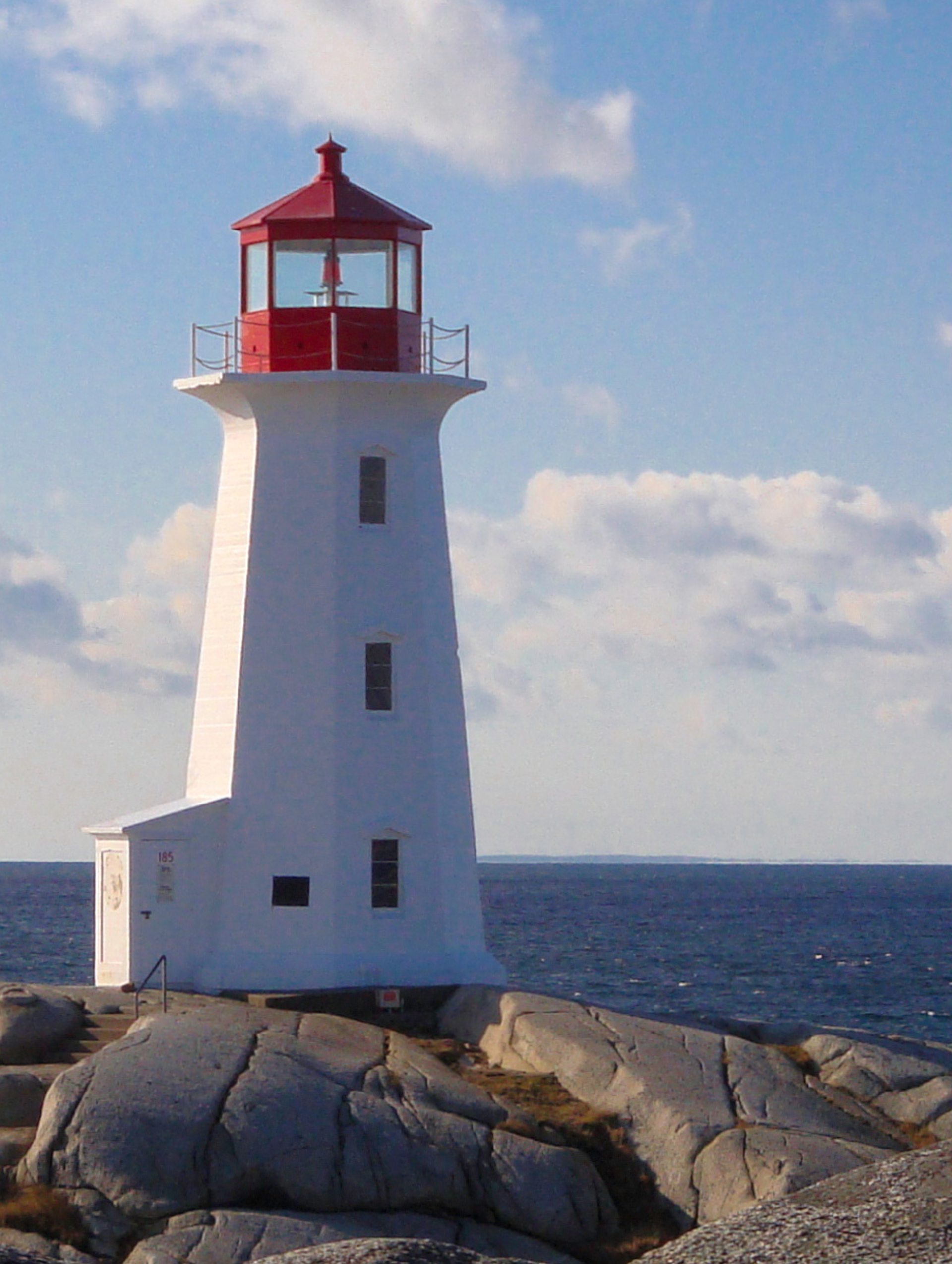 A white lighthouse with a red top sits on a rock near the ocean