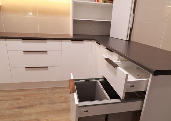 A kitchen with white cabinets and a trash can in the drawer.