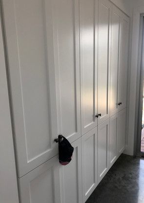 A black hat is hanging on the door of a white cabinet.