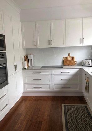 A kitchen with white cabinets and hardwood floors.