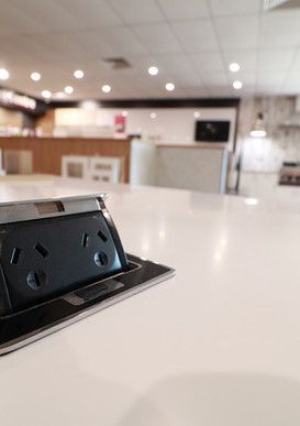 A black electrical outlet is sitting on top of a white counter in a kitchen.