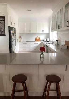 A kitchen with white cabinets and stools and a vase of flowers on the counter.