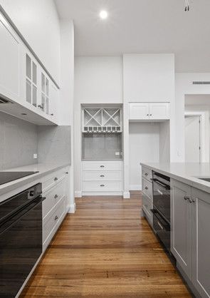 A kitchen with white cabinets, black appliances, wooden floors and a wine rack.